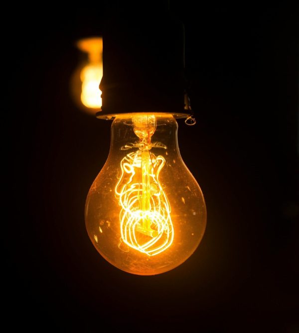 Close-up view of an illuminated vintage light bulb with glowing filament against a dark background.